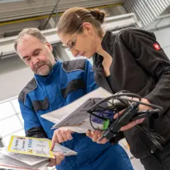 Mitarbeiter besprechen Dokumente zur Auffrischung Sicherheitsbeauftragter in einer Werkstatt.