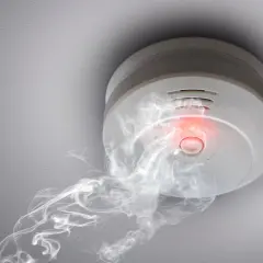 Rauchmelder mit rotem Licht und Rauch, der darauf hindeutet, wie viele Rauchmelder im Haus wichtig sind.