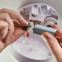 Hände wechseln die Batterie eines Rauchmelders, da die alte leer ist. Sicherheit geht vor!