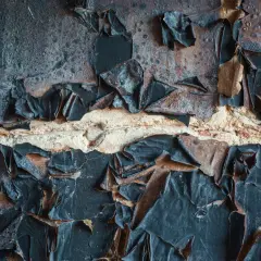 Abgeblätterte schwarze Farbe auf einer Ziegelwand, die auf eine Schadstoffmessung nach Brand hindeutet.
