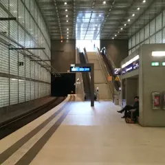 Moderne U-Bahn-Station mit Glaswänden, Rolltreppen und einer Uhr. Die Notbeleuchtung ist gemäß Vorschriften installiert.