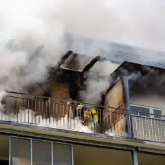 Feuerwehrleute kämpfen gegen einen Wohnungsbrand. Rauch quillt aus dem Gebäude. Ein Albtraum ohne Hausratversicherung.