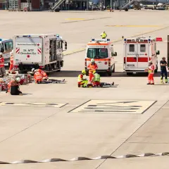 Einsatzkräfte von Feuerwehr und Katastrophenschutz üben am Flughafen. Mehrere Einsatzfahrzeuge, darunter ein Löschzug, sind vor Ort.
