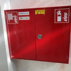 Roter Schrank für Brandschutz in einer Arztpraxis: Wandhydrant Typ F, 200 l/min, und Feuerlöscher-Symbol.