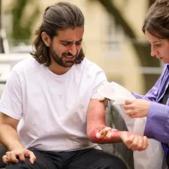 Frau versorgt mit einem Tuch die schmerzhafte brandwunde am Arm eines Mannes.