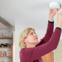 Frau montiert Rauchmelder nach DIN 14676 an der Decke.