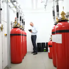 Mann prüft Brandschutz-System im Serverraum. Rote Gasflaschen sind für den Ernstfall bereit.