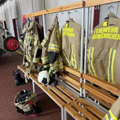 Schutzkleidung für die ehrenamtliche Feuerwehr hängt bereit. Stiefel und Helme liegen auf der Bank.