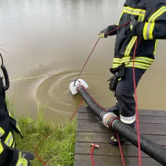 Feuerwehrleute führen eine wasserentnahme offenes gewässer fwdv 3 durch. Ein Tauchpumpen-Ansaugschlauch wird ins trübe Wasser gelassen.