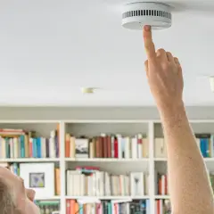 Mieter prüft Rauchmelder. Regelmäßige Rauchmelder Wartung ist wichtig für Haus und Grund. Vordrucke helfen bei der Dokumentation.