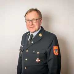Mann in Uniform mit Orden und Aufnäher "Freiwillige Feuerwehr". Sein Kreisbrandrat Gehalt ist wohl angemessen für diese Verantwortung.