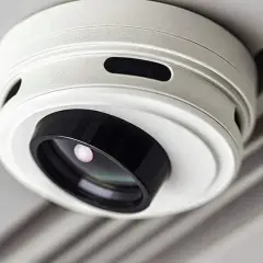 Ein weißer Rauchmelder mit integrierter Kamera, der unauffällig an der Decke montiert ist. Er hilft, Rauch zu erkennen und gleichzeitig die Umgebung zu überwachen.