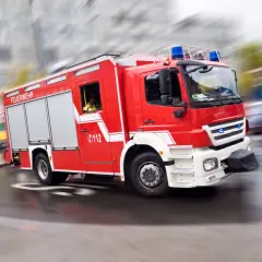 Rotes Feuerwehrauto mit Blaulicht rast durch die Stadt. Ein Feuerwehrmann am Steuer, bereit für den Einsatz. Rauchmelder sind wichtig, aber die Feuerwehr ist die ultimative Rettung.