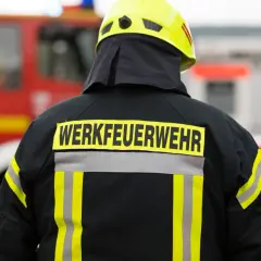 Rückansicht eines Feuerwehrmanns mit gelbem Helm und Jacke, auf der "WERKFEUERWEHR" steht. Dies zeigt, was eine Werkfeuerwehr ist: eine spezialisierte Feuerwehr für Industriebetriebe.