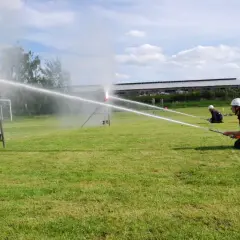 Feuerwehrleute üben einen löschangriff nass aufbau. Sie zielen mit Wasserschläuchen auf Ziele auf einem Feld.