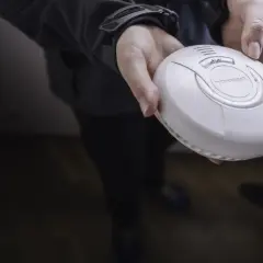 Eine Hand hält einen weißen Rauchwarnmelder. Dieses Gerät ist wichtig für die Sicherheit zu Hause.