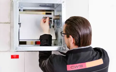 Techniker prüft die brandschutzklappe funktion. Er justiert eine Feder im Metallgehäuse, um die Sicherheit zu gewährleisten.