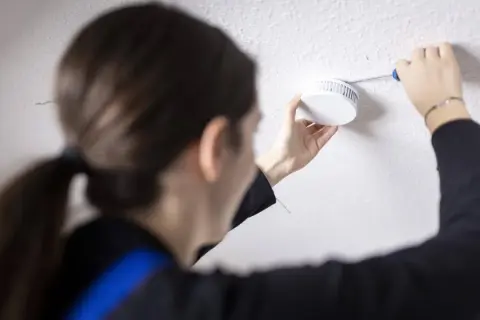 Frau tauscht Rauchmelder aus, da die Frist abgelaufen ist. Sicherheit geht vor!