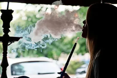 Silhouette einer Frau, die eine Shisha raucht. Dichter Rauch steigt auf und umhüllt ihr Gesicht. Ein **Rauchmelder** wäre hier fehl am Platz.