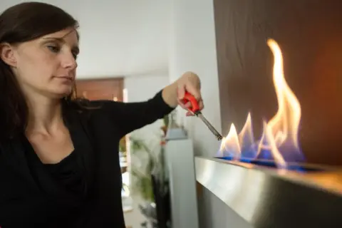 Frau zündet Ethanol-Kamin an. Die Flammen tanzen, ein Zeichen für Wärme und Gemütlichkeit, dank der Ethanol-Marke.