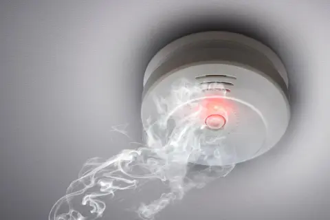 Rauchmelder mit rotem Licht und Rauch, der darauf hindeutet, wie viele Rauchmelder im Haus wichtig sind.
