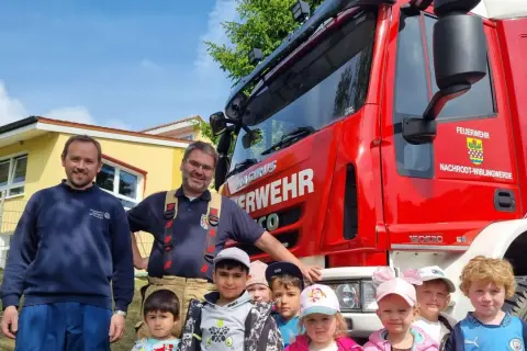 Feuerwehrleute und Kinder vor einem roten Feuerwehrauto. Ein fröhlicher Tag der Feuerwehr!