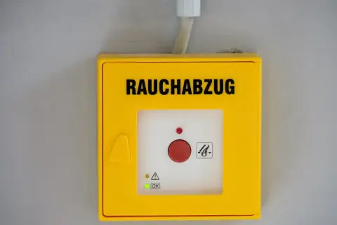 Gelbes Gehäuse für Rauchabzug mit rotem Knopf. Ein grünes Licht zeigt "OK" an, was auf ein erfolgreiches Wartungsprotokoll RWA Muster hindeutet.