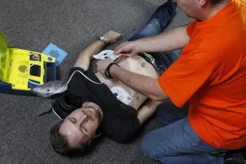 Mann legt Elektroden eines Defibrillators an, um Leben zu retten. Wann Defibrillator? Jetzt!