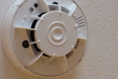Ein weißer Rauchmelder mit integrierter Kamera, der an einer Decke montiert ist.