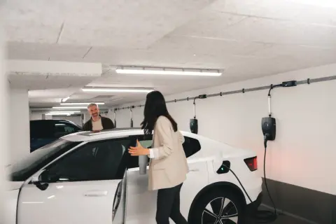 Frau und Mann in Tiefgarage bei Wallbox-Ladestation. Brandschutz ist hier wichtig, während das Elektroauto geladen wird.