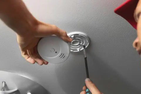 Mann schraubt Rauchmelder an Decke. Einfache Rauchmelder Wandmontage für mehr Sicherheit.