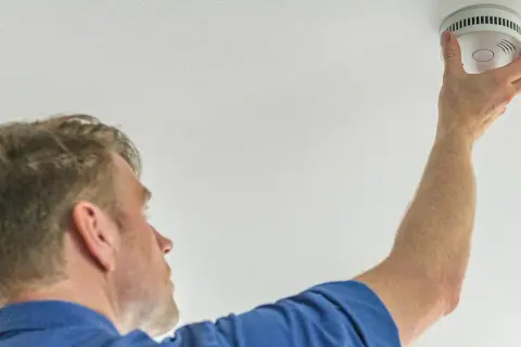 Mann montiert Rauchmelder an der Decke. In Bremen ist die Rauchmelderpflicht für Wohnungen gesetzlich vorgeschrieben.