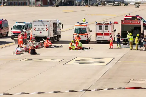 Einsatzkräfte von Feuerwehr und Katastrophenschutz üben am Flughafen. Mehrere Einsatzfahrzeuge, darunter ein Löschzug, sind vor Ort.