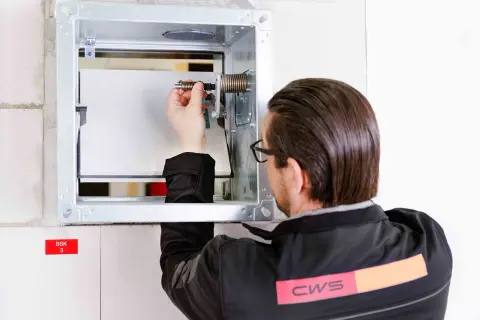 Techniker prüft die brandschutzklappe funktion. Er justiert eine Feder im Metallgehäuse, um die Sicherheit zu gewährleisten.