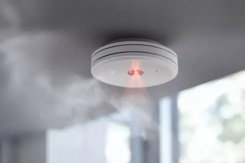 Rauchmelder mit rotem Licht und Dampf. Ein Fehlalarm bei Rauchmeldern kann teuer werden, aber Sicherheit geht vor.