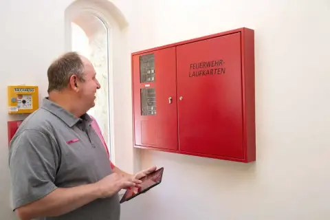 Mann prüft mit Tablet die Brandmeldeanlage. Regelmäßige Wartung sorgt für Sicherheit.