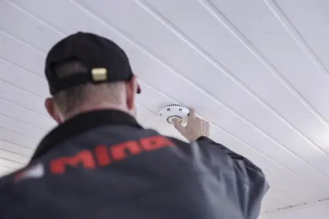 Ein Mann mit Kappe montiert einen kalo rauchmelder an der Decke.