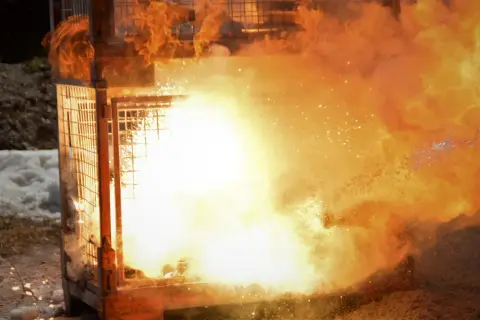 Ein Metallkäfig wird von einer gewaltigen Explosion aus Feuer und Rauch erfasst. Es ist beeindruckend zu sehen, dass metall brennen kann.