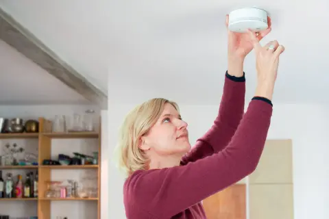 Frau montiert Rauchmelder nach DIN 14676 an der Decke.