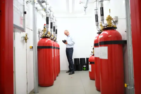 Mann prüft Brandschutz-System im Serverraum. Rote Gasflaschen sind für den Ernstfall bereit.