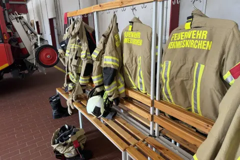 Schutzkleidung für die ehrenamtliche Feuerwehr hängt bereit. Stiefel und Helme liegen auf der Bank.