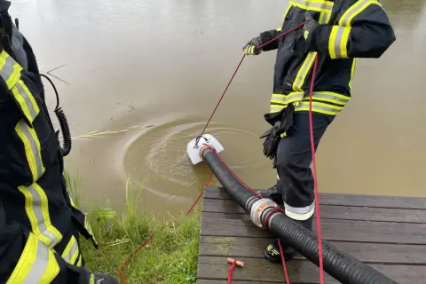 Feuerwehrleute führen eine wasserentnahme offenes gewässer fwdv 3 durch. Ein Tauchpumpen-Ansaugschlauch wird ins trübe Wasser gelassen.