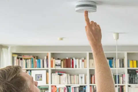 Mieter prüft Rauchmelder. Regelmäßige Rauchmelder Wartung ist wichtig für Haus und Grund. Vordrucke helfen bei der Dokumentation.