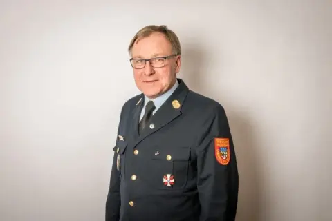 Mann in Uniform mit Orden und Aufnäher "Freiwillige Feuerwehr". Sein Kreisbrandrat Gehalt ist wohl angemessen für diese Verantwortung.