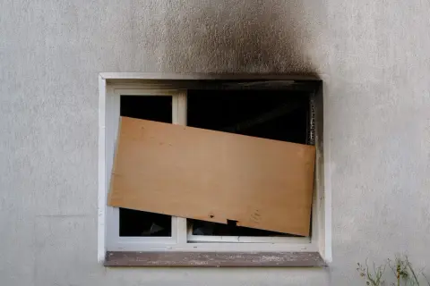 Beschädigtes Fenster, provisorisch mit Holzplatte verschlossen. Die Frage, wie lange bleibt eine Wohnung versiegelt, bleibt offen.