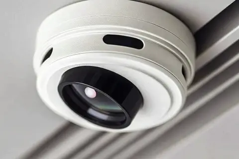 Ein weißer Rauchmelder mit integrierter Kamera, der unauffällig an der Decke montiert ist. Er hilft, Rauch zu erkennen und gleichzeitig die Umgebung zu überwachen.