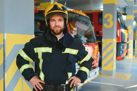 Ein Feuerwehrmann im Einsatz, bereit für seinen wichtigen Beruf. Im Hintergrund stehen Einsatzfahrzeuge in einer Garage.