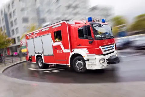 Rotes Feuerwehrauto mit Blaulicht rast durch die Stadt. Ein Feuerwehrmann am Steuer, bereit für den Einsatz. Rauchmelder sind wichtig, aber die Feuerwehr ist die ultimative Rettung.