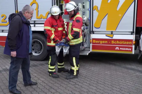 Zwei Feuerwehrmänner mit Rettungsgerät, ein Mann in Zivil. Frage: ab wann darf man bei der freiwilligen feuerwehr einsätze mitfahren?