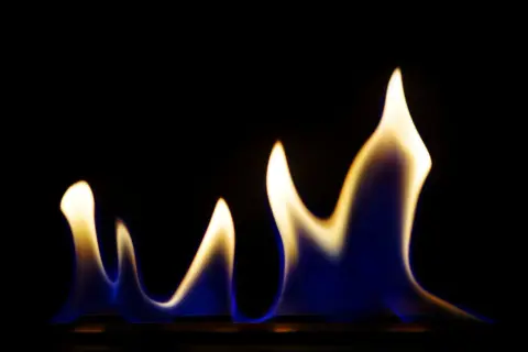 Blau-gelbe Flammen tanzen im Dunkeln, eine Warnung vor den ethanol gefahren.